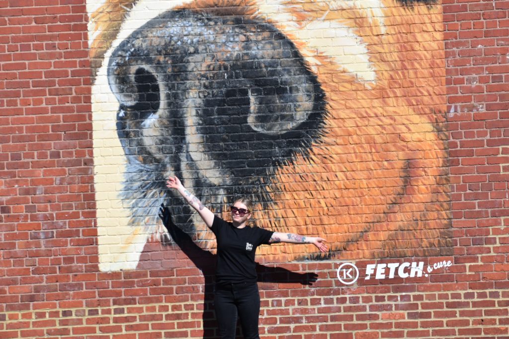 girl with arms open wide standing in front of dog mural